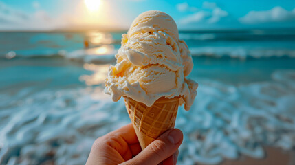 Hand holding an ice cream cone or cornet against a backdrop of the sea and beach at sunset