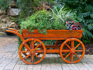 An orange flower cart made of wood with four large wheels placed at a public park.