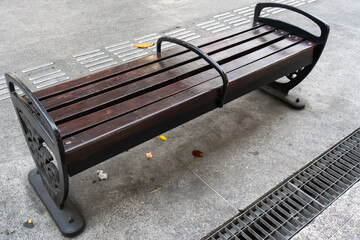 A park bench made of black metal and dark brown wood nailed to the concrete sidewalk near a small sewer channel.