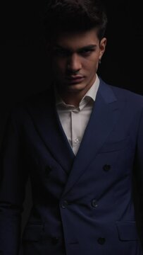 classy businessman in double breasted blue suit standing on black background with strobes effect and looking sexy
