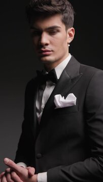 closeup of handsome fashion man in black tuxedo holding palms together while standing and moving on black background