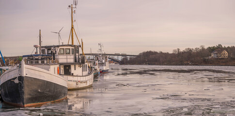 Panorama, bay in the lake Mälaren with ice floe, jetty with old wood fishing boats a gray winter in Stockholm