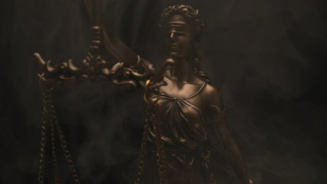 project video of blindfolded bronze law statue holding a scale in front of black background with smoke and police lights, concept of right and wrong