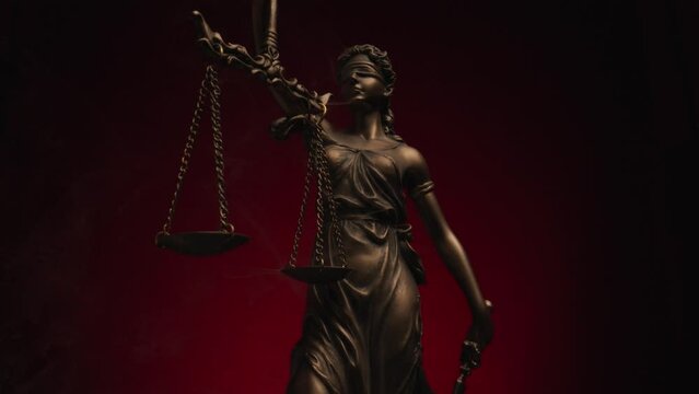 project video of bronze law statue symbolizing the concept of equality with scale in her hands in front of black background with red background and smoke