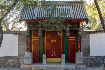 A traditional Chinese gate with concrete roof and densely ornamental upper section, two doors with...