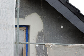A wall of a house covered with EPS graphite polystyrene boards for thermal insulation, a window covered with a protective film, a scaffolding, anchors