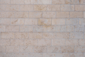texture of a tiled beige stone wall as background, natural stone wall texture as background. Close-up of a wall clad in limestone	