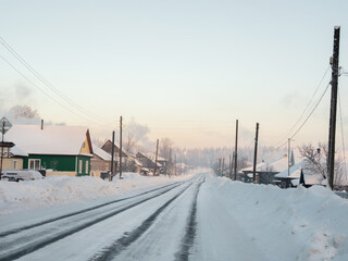 Winter road through a snow-covered village, severe frost, snow haze