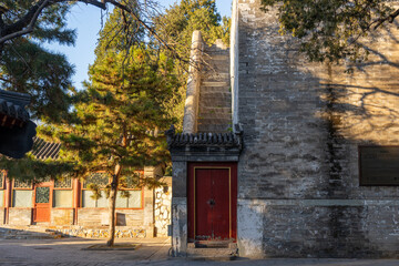 A red door with Chinese architectural design leading to a stone staircase with an outer wall that...