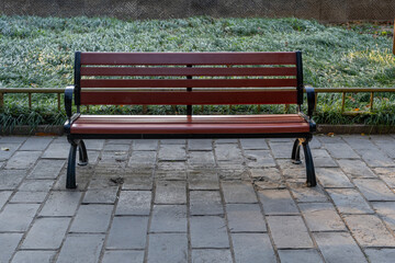 A front view of a park bench made of dark brown hard wood and black metal frame on a stone pavement at a Chinese palace park complex.