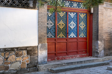 A close up view of an entrance to a traditional upper class Chinese house with dominant red color and blue carvings for an artistic architectural design.