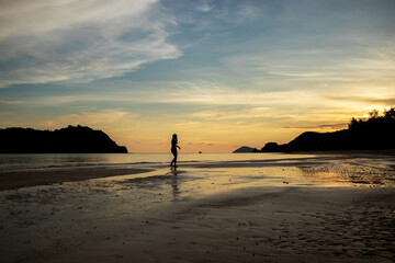 one silhouette of a woman walking on the beach at sunset