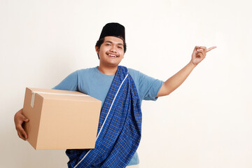 Happy asian muslim boy standing pointing sideways while carrying a package