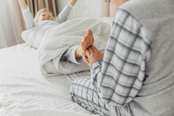 the children are wrapped in a blanket and tickling each other's heels on the bed. Family having fun at home. Leisure