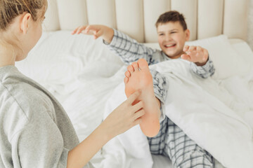 Fototapeta premium the children are wrapped in a blanket and tickling each other's heels on the bed. Family having fun at home. Leisure