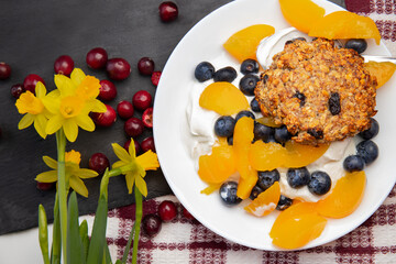 Healthy oatmeal cookies for breakfast, served with peaches, blueberries and natural yogurt. There are daffodil flowers on the table next to the Healthy dessert.