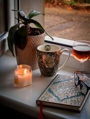 Still life with a candle, a mug and a glass of wine on a window sill