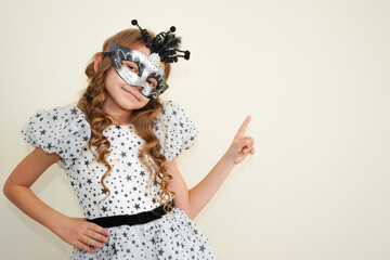 Child in a carnival masquerade mask. Festival, carnival, party. A little girl makes faces in a...