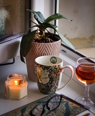 Still life with a candle, a mug and a glass of wine on a window sill