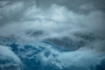 Foggy winter landscape with snow-covered mountains and clouds in the background