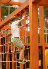Little boy climbing on a rope ladder in a children's playground