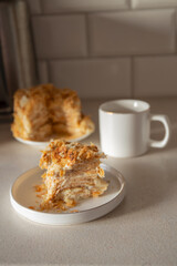 A slice of Napoleon cake on a white dessert plate on the kitchen table, part of homemade baking preparations.