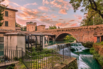 view of Bevagna, Umbria, Italy, with bridge, canal of the old mills and waterfalls - 727708512