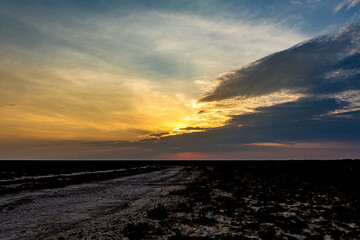 Obraz premium Sunrise or sunset on the salt lake Bulukhta (Russia). Steppe road from salt marsh. The sun is hiding behind Cirrostratus or Cumulostratus clouds in the morning or evening.