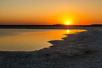 Sunset or sunrise on salt lake Baskunchak (Russia). Bright sun in a cloudless sky, calm brine in the saline. Morning or evening in summer, autumn or spring.