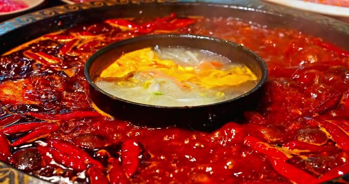 Chinese spicy hot pot cuisine. A layer of red chili pepper floats in the boiling hot pot base. 4K Real time video.