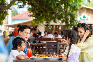 Happy Asian family enjoy and fun outdoor lifestyle travel and having dinner at tropical island beach on summer holiday vacation. Parents and little kids eating sea food together at beach restaurant.