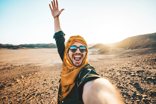 Happy traveler with backpack taking selfie picture with smart mobile phone outdoors - Cheerful guy smiling on the top of the mountain - Hiker traveling in rocky desert - Travel technology life style