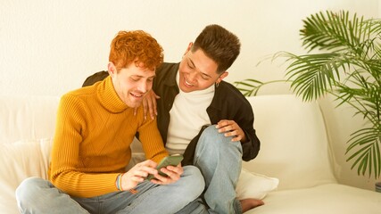 Gay couple smiling while using the mobile at home