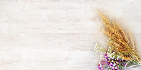 Ripe yellow wheat bouquet with purple and white flowers, on a white wooden surface. Intended for a...