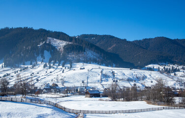 Landscape with a mountain village in winter. Houses spread out on a slope in the countryside covered with snow