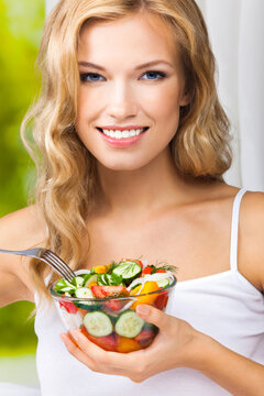 Portrait image - happy smiling young blond blonde woman holding glass bowl with vegetable salad home house interior, indoors. Healthy eating, vegetarian, keto ketogenic diet concept.