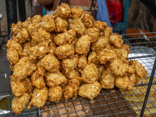 A pile of freshly fried vegetable tempura, or Bakwan, served for sale on a metal web case at a street food stall.