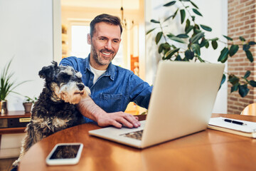 Happy man at home using laptop sitting together with his dog