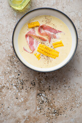 Bowl of corn chowder with bacon on a beige granite background, vertical shot, copy space, above view