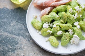 Closeup of potato gnocchi with green pea sauce, feta cheese and bacon, horizontal shot on a grey granite background, selective focus