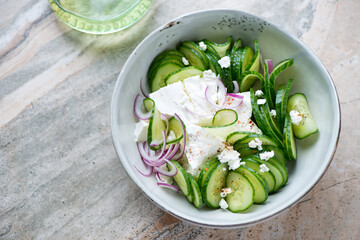 Bowl of cucumber and feta cheese salad, horizontal shot on a light-grey granite background, elevated view