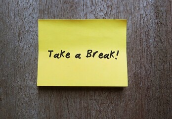 Yellow note on copy space gray wall with text handwritten TAKE A BREAK, concept of self reminder to relax, stress free , stay out of conflict