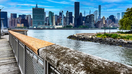 View of the New York skyline from the stone cliff pier and overlook of Long Island which is a large island that extends from the east of the Big Apple and Manhattan (USA). - Powered by Adobe