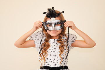 Child in a carnival masquerade mask. Festival, carnival, party. A little girl makes faces in a mask. Black and silver mask. Theater. Children's theater. Home theater. Performance for children. 