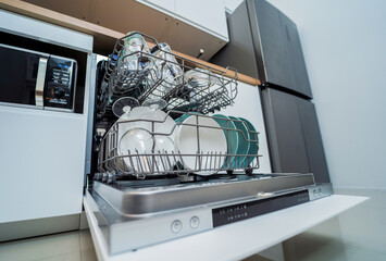 The white kitchen and opened dishwasher with clean dishes
