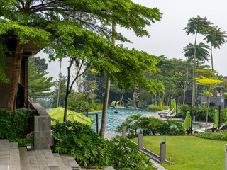 A tranquil swimming pool garden of a five-star hotel with canopies, chaises, trees, and well maintained green grass.