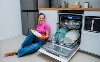 Young woman sitting on the floor near the dishwasher machine