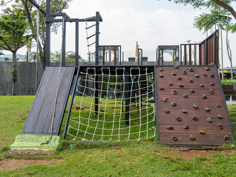An outdoor children jungle gym with multiple climbing challenges: rope-aided slide, rope ladder, and a rock climbing wall, built on a green backyard of a five-star hotel.