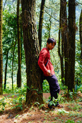 Naklejka na ściany i meble Javanese man in red is leaning against a tree in the forest. 