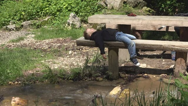 Little child lying down to rest on wooden bench in nature